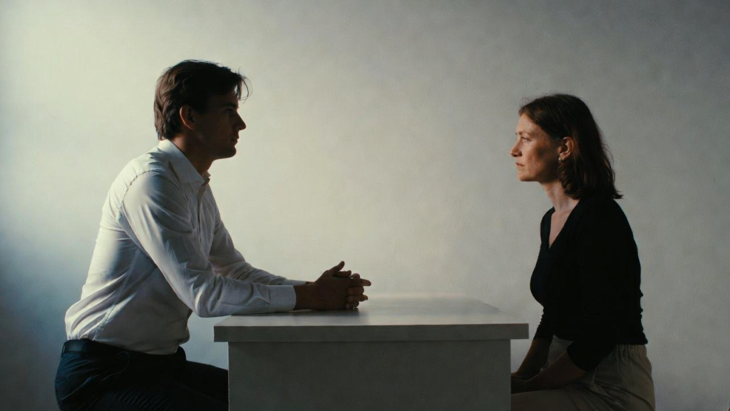 The Silent Patient by Alex Michaelides - What Makes This a Bestseller? a fromally dressed man and a woman sitting on the opposite sides of a table, facing each other