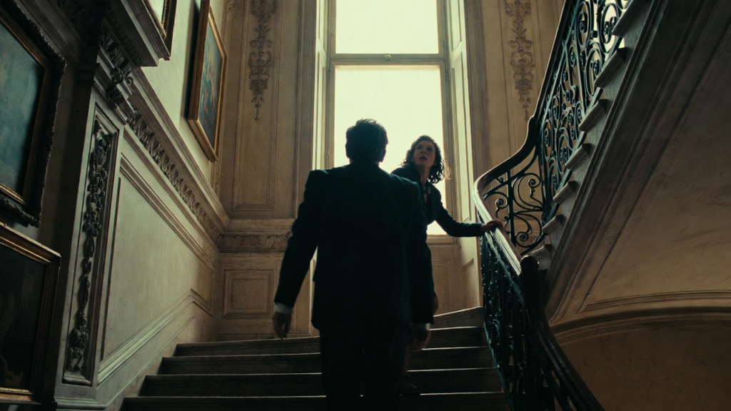 a man and a woman climbing up a staircase in a mansion